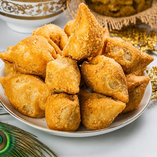 Plate of crispy golden samosas with a peacock feather and decorative bowl.