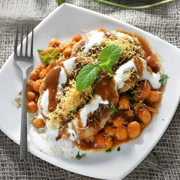Indian dish with chickpeas, yogurt, tamarind chutney, mint, and crispy sev on a white plate.